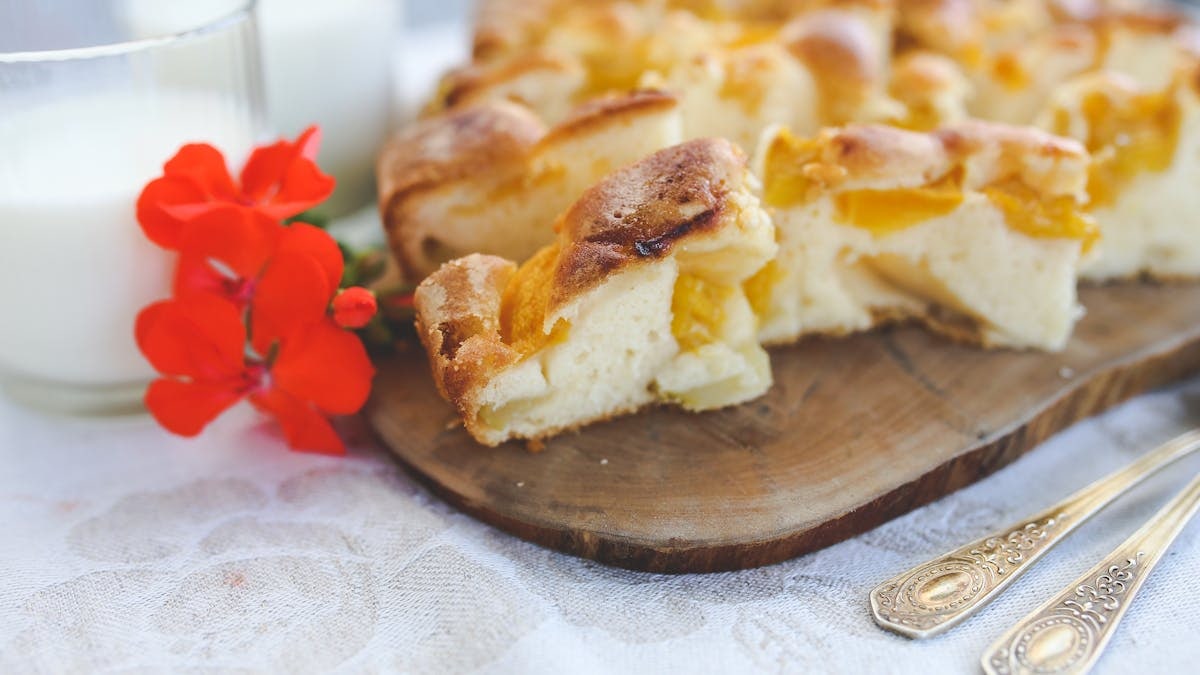Slice of homemade peach pie on wooden board with milk and red flowers.